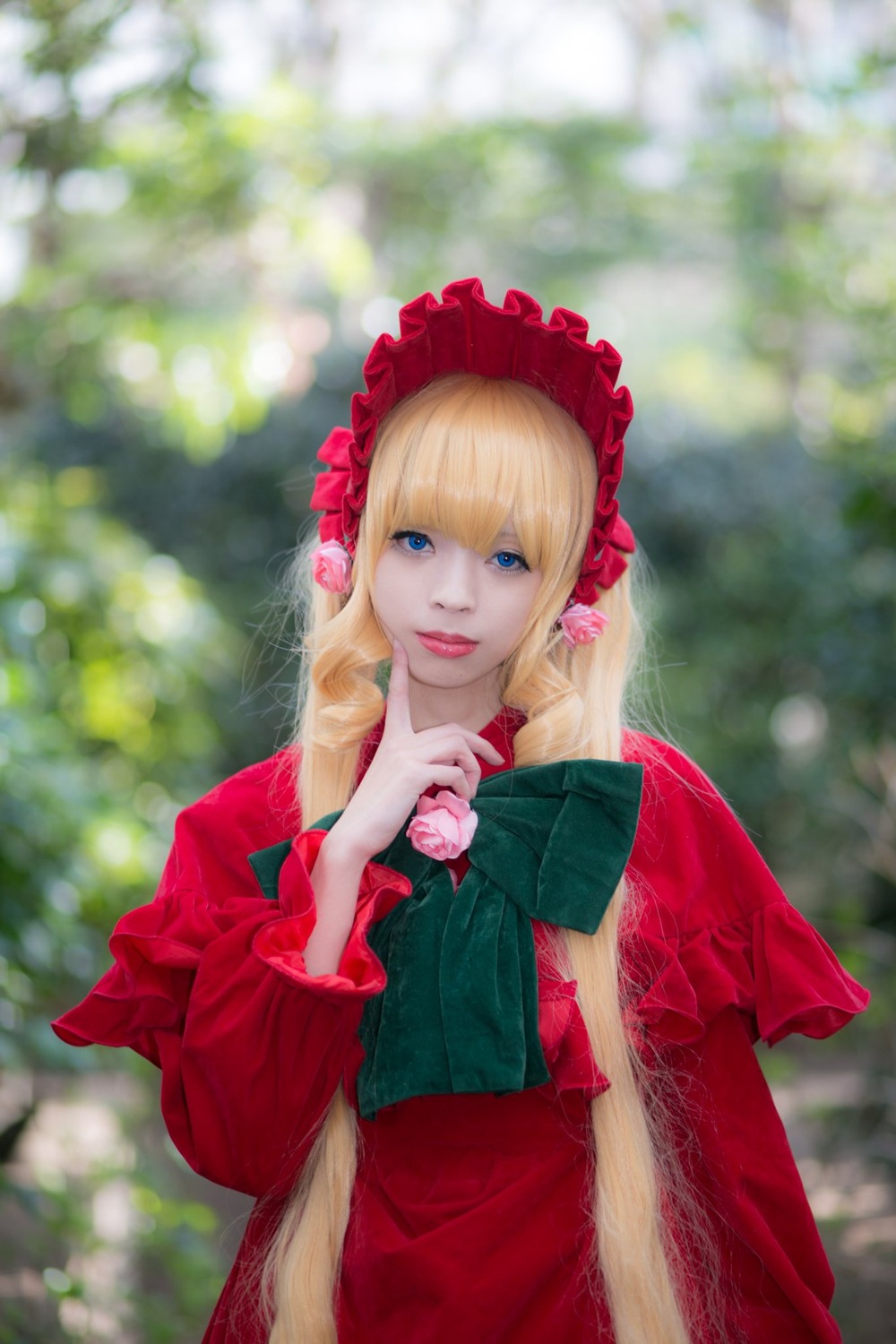 1girl bangs blonde_hair blue_eyes blurry blurry_background bonnet bow capelet depth_of_field dress flower lips long_hair long_sleeves looking_at_viewer photo red_dress red_flower rose shinku smile solo