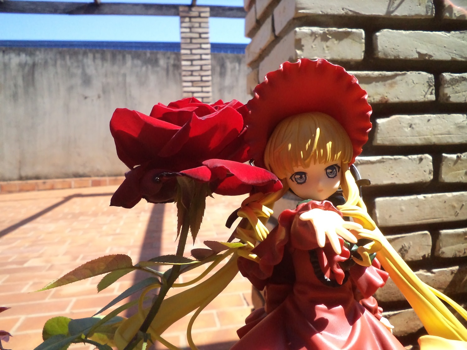 1girl bangs blonde_hair blue_eyes bonnet day doll dress drill_hair flower frills hat long_hair long_sleeves looking_at_viewer outdoors railing red_dress shinku solo standing twintails very_long_hair