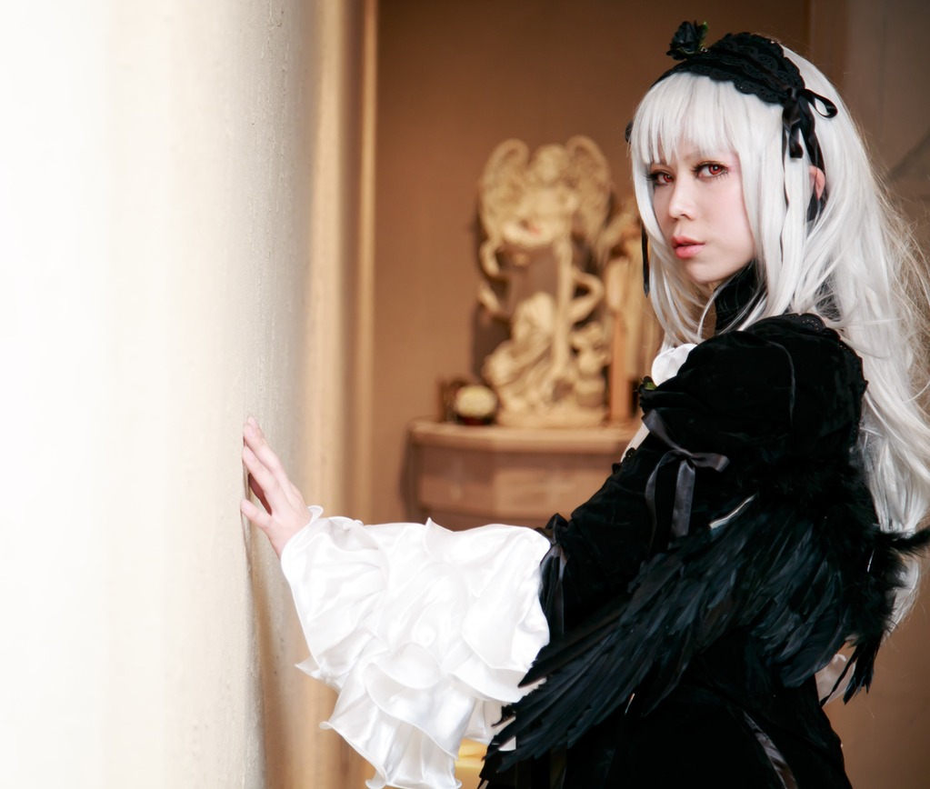 1girl black_wings blurry blurry_background depth_of_field dress frills gothic_lolita hairband juliet_sleeves long_hair long_sleeves looking_at_viewer photo red_eyes rose sitting solo suigintou wings