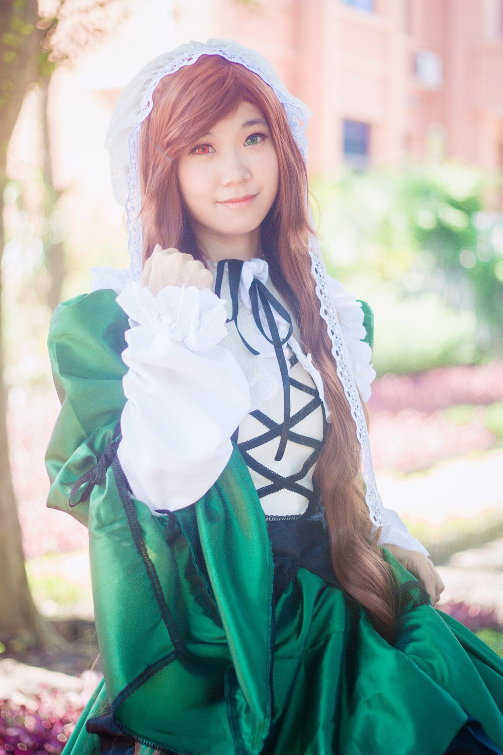 1girl bangs blurry blurry_background brown_hair depth_of_field dress frills green_dress heterochromia lips long_hair long_sleeves looking_at_viewer outdoors red_eyes ribbon smile solo suiseiseki