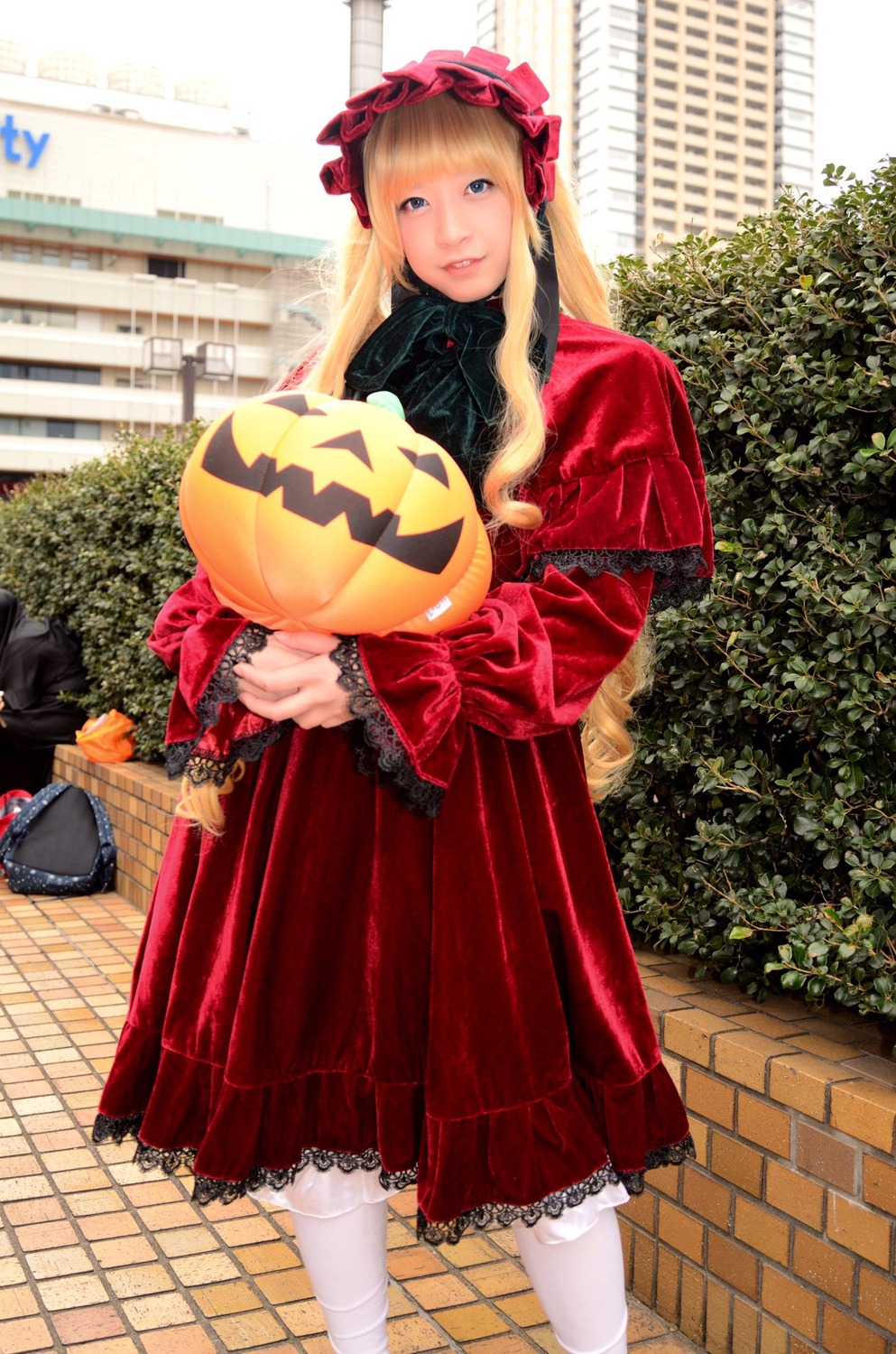 1girl blonde_hair blue_eyes bonnet bow chain-link_fence dress fence frills jack-o'-lantern lolita_fashion long_hair long_sleeves looking_at_viewer outdoors pavement pumpkin red_dress shinku solo standing white_legwear