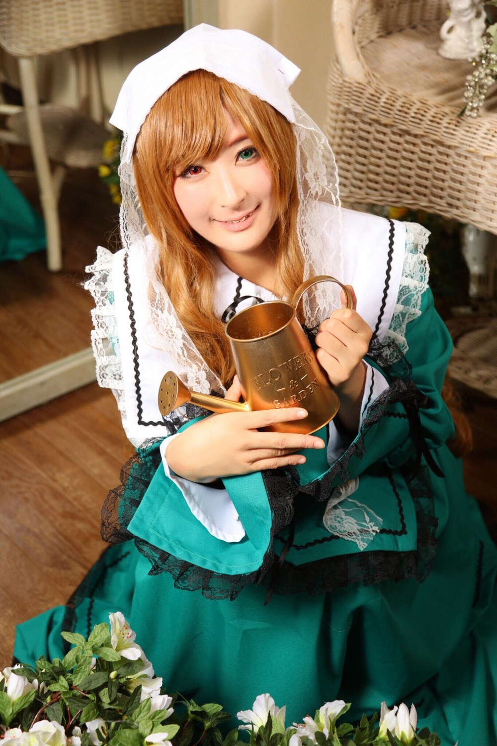 1girl blonde_hair blurry cup depth_of_field dress flower frills green_dress green_eyes heterochromia holding lace lips long_hair looking_at_viewer red_eyes sitting smile solo suiseiseki