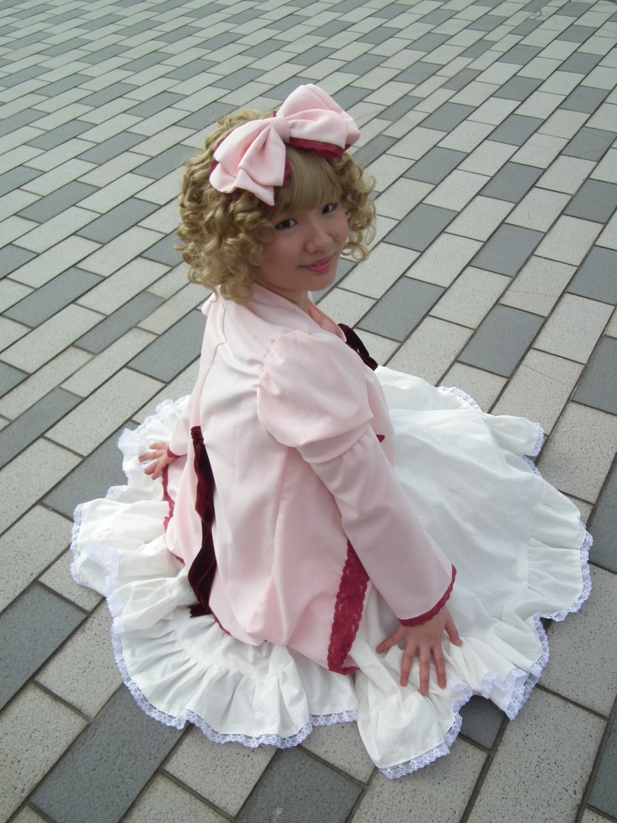 1girl blonde_hair blue_eyes bow brick_wall checkered checkered_floor curly_hair dress frills hair_bow hinaichigo lips looking_at_viewer looking_back sitting solo tile_floor tile_wall tiles white_dress