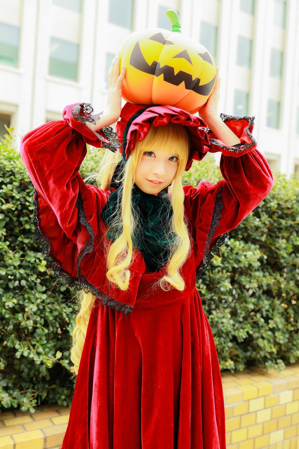 1girl arms_up bangs blonde_hair blue_eyes bonnet building day dress jack-o'-lantern long_hair long_sleeves looking_at_viewer outdoors red_dress shinku smile solo standing