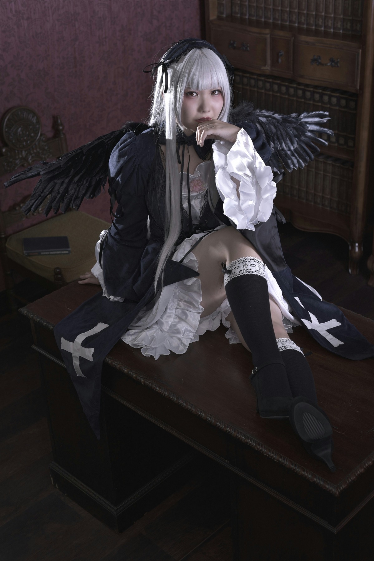 1girl black_wings boots doll_joints dress feathered_wings feathers frills gothic_lolita indoors kneehighs long_hair ribbon sitting solo suigintou white_hair wings