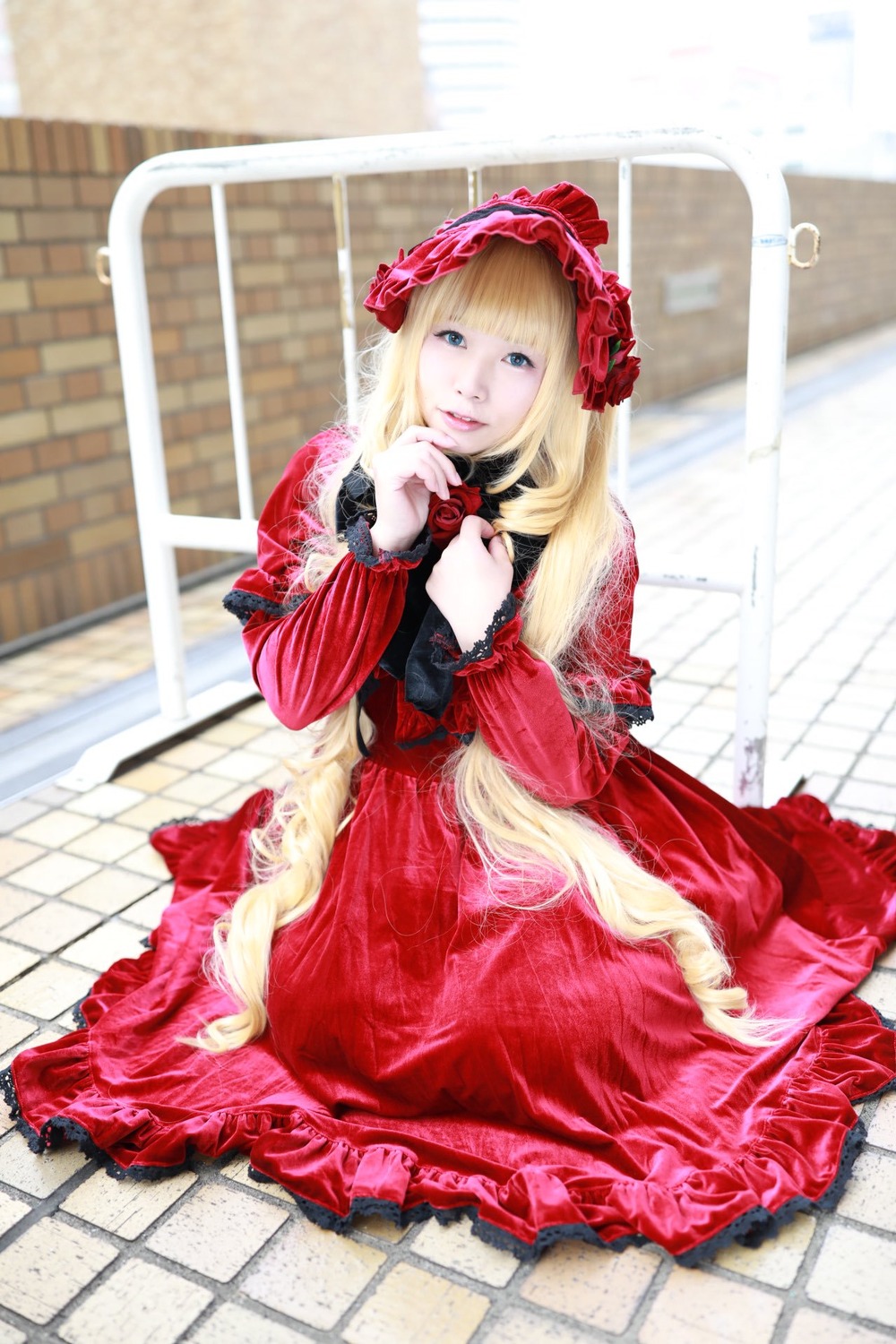 1girl blonde_hair blue_eyes blurry bonnet chain-link_fence depth_of_field dress fence flower frills long_hair long_sleeves photo red_dress rose shinku sitting solo tile_floor tiles