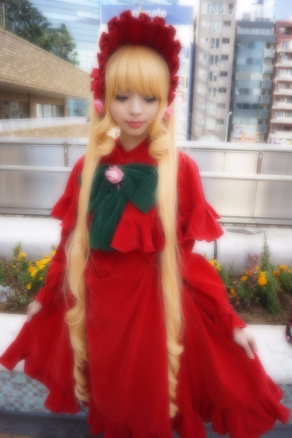 1girl blonde_hair blurry bonnet building day dress flower long_hair long_sleeves outdoors red_dress shinku solo standing