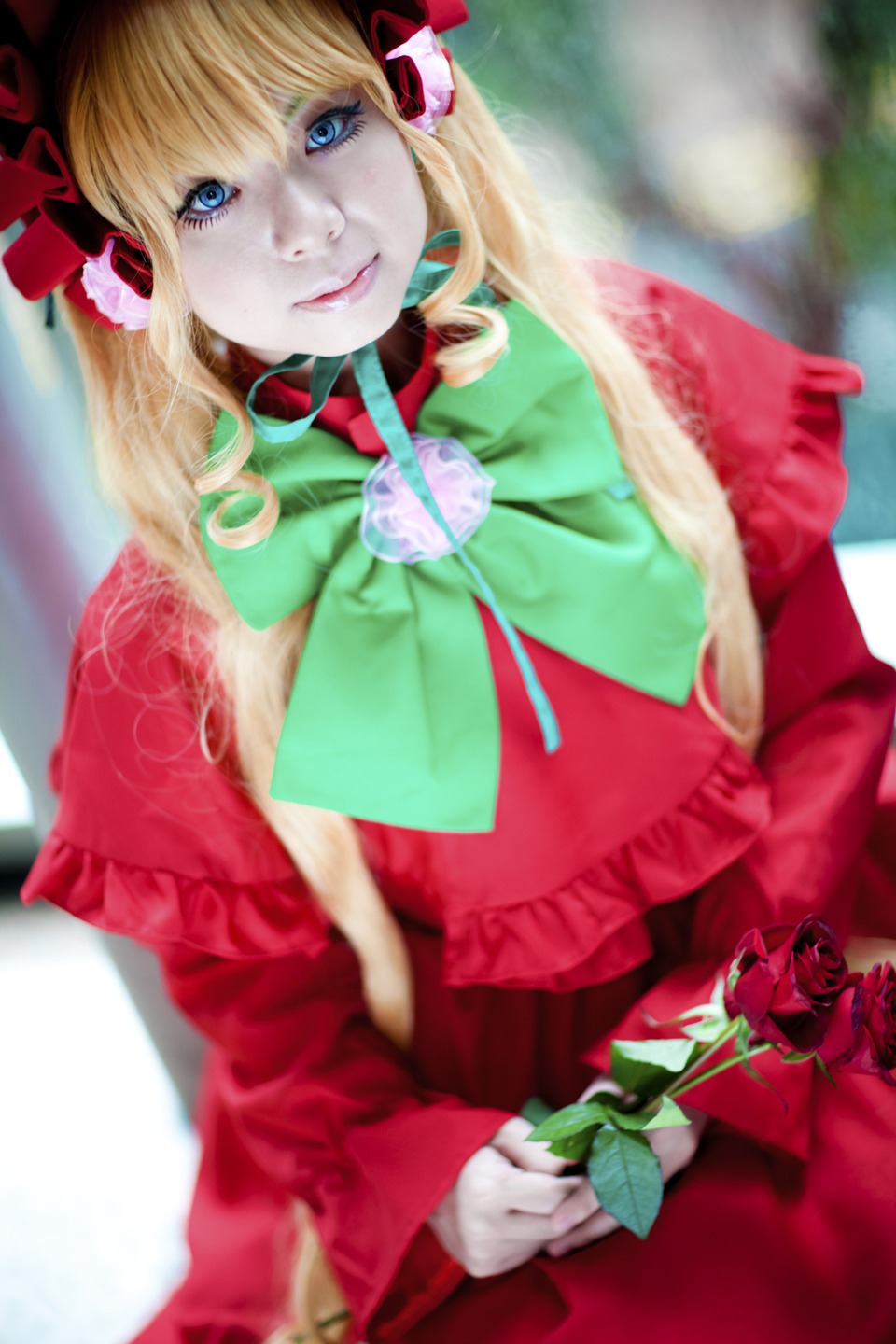 1girl blonde_hair blue_eyes blurry blurry_background bow capelet depth_of_field dress flower green_bow lips long_hair looking_at_viewer red_capelet ribbon rose shinku solo