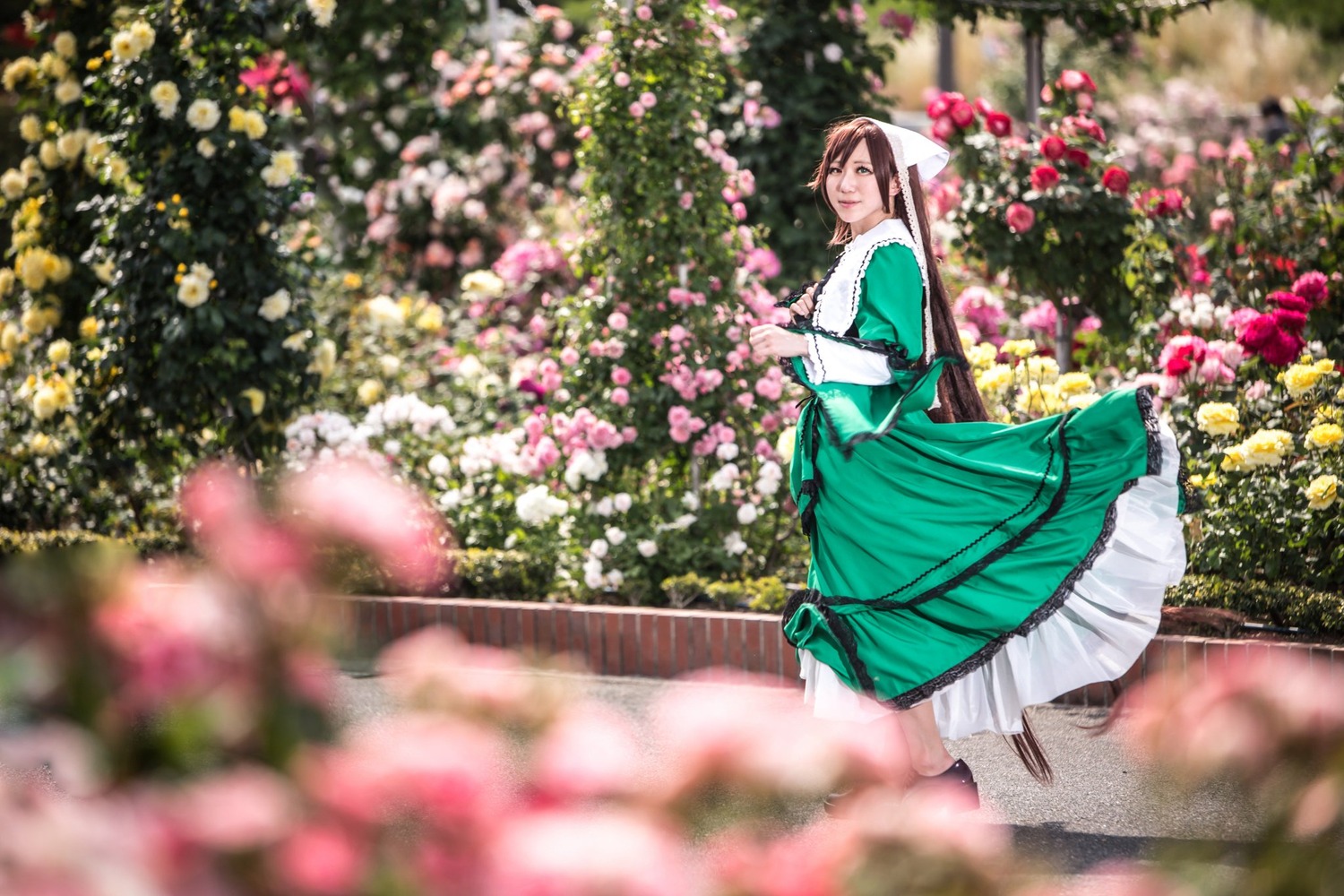 1girl blue_dress blurry blurry_foreground brown_hair depth_of_field dress flower frills green_dress long_hair long_sleeves motion_blur outdoors solo standing suiseiseki