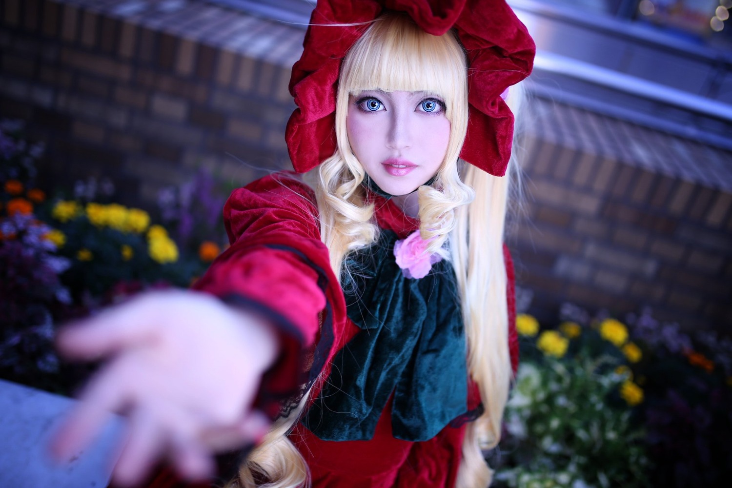 1girl bangs blonde_hair blue_eyes blurry blurry_background blurry_foreground depth_of_field doll_joints dress flower foreshortening giving hood lips looking_at_viewer outdoors outstretched_arm reaching_out red_dress rose shinku solo