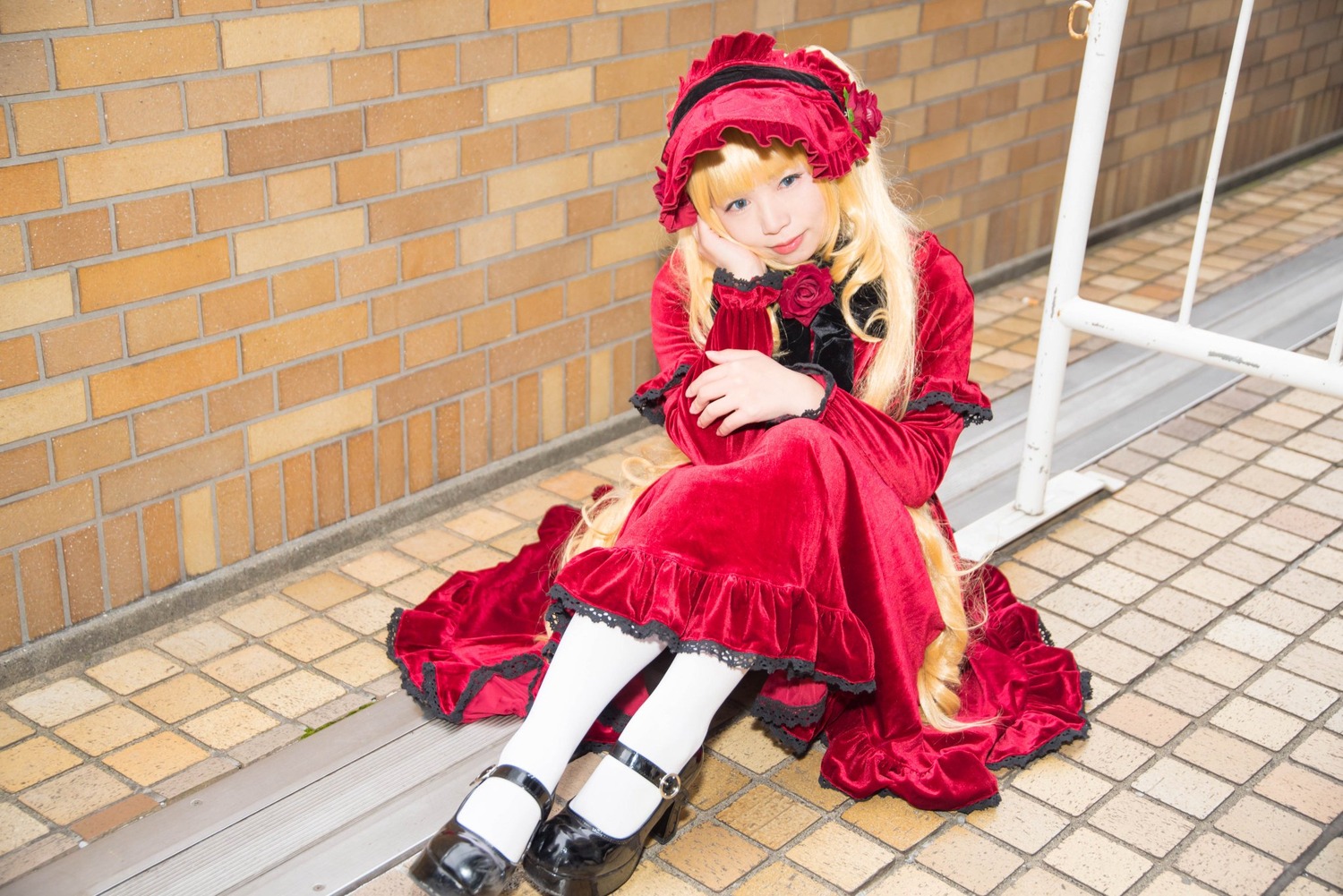 1girl blonde_hair blue_eyes bonnet brick_wall chain-link_fence dress fence floor flower long_hair long_sleeves looking_at_viewer pantyhose pavement red_dress rose shinku shoes sitting solo tile_floor tile_wall tiles wall white_legwear