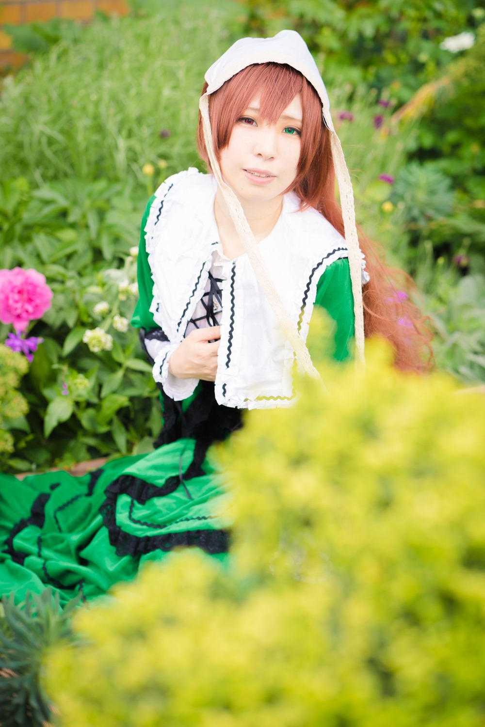 1girl apron bangs blurry blurry_background blurry_foreground brown_hair crossed_arms depth_of_field dress flower green_eyes head_scarf lips long_hair outdoors photo smile solo suiseiseki