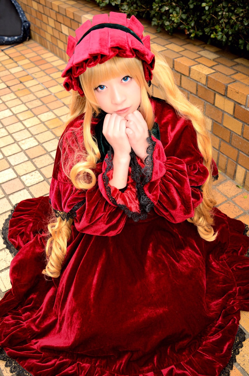 1girl blonde_hair blue_eyes bonnet brick_wall chain-link_fence dress frills hands_together lolita_fashion long_hair long_sleeves looking_at_viewer red_dress shinku smile solo tile_floor tiles