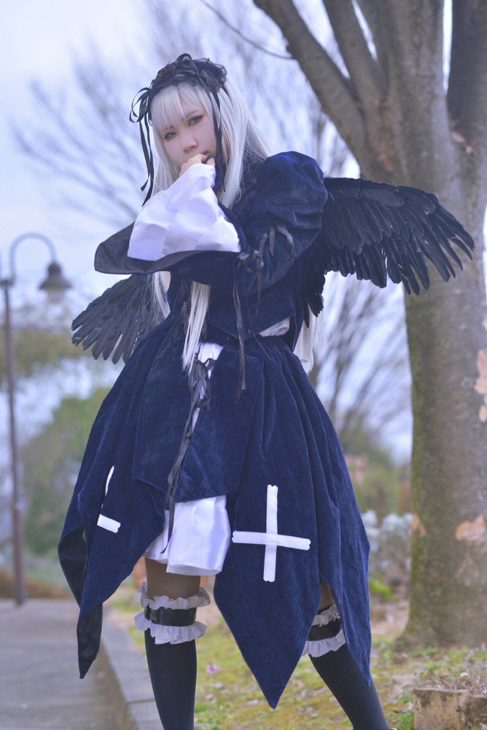 1girl bangs black_dress black_wings blurry blurry_background blurry_foreground depth_of_field dress feathered_wings hairband long_hair long_sleeves looking_at_viewer outdoors ribbon silver_hair solo standing suigintou wings