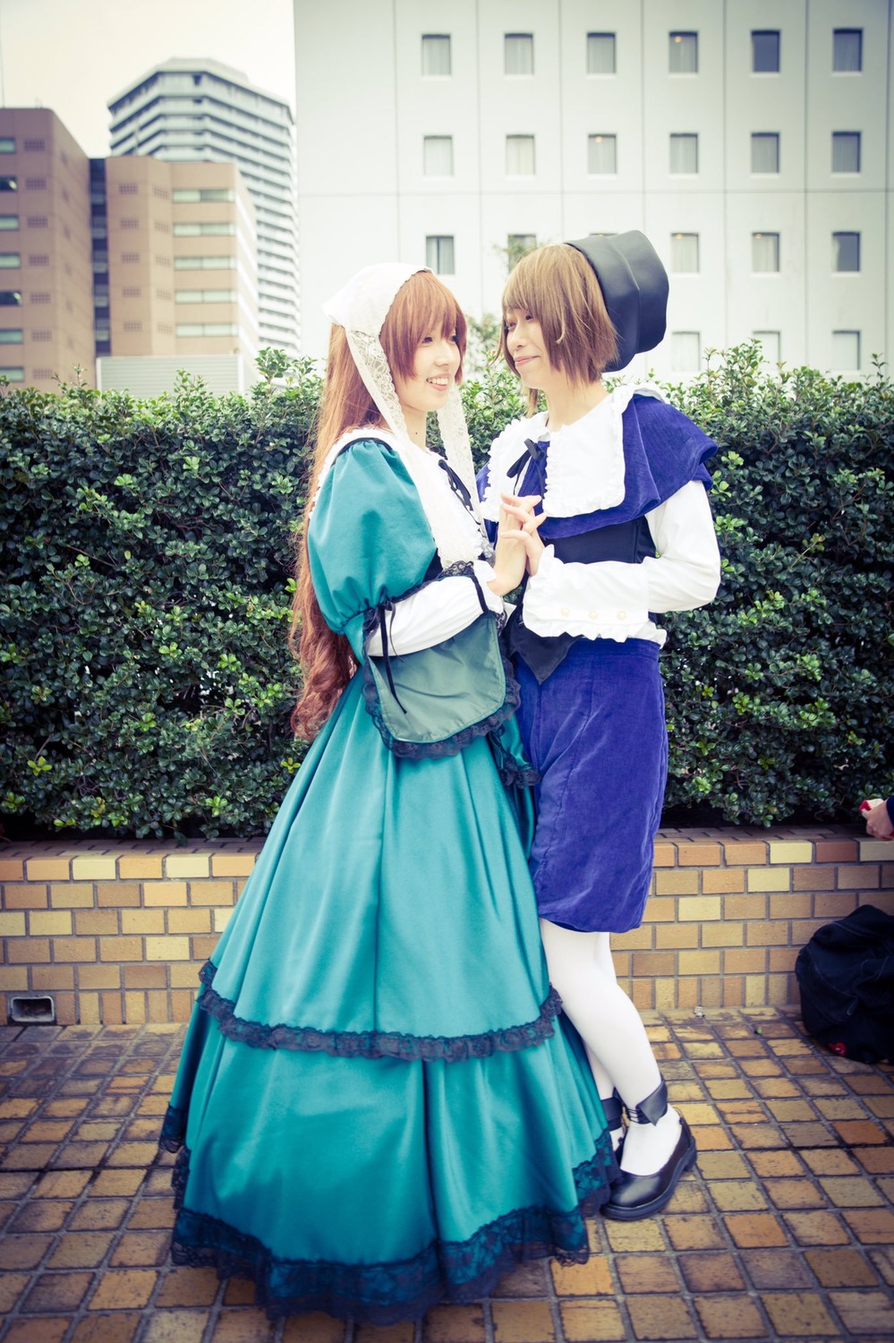 apron blonde_hair blue_dress brick_wall brown_hair building chain-link_fence closed_eyes dress hat holding_hands long_hair multiple_cosplay outdoors pantyhose pavement shoes standing tagme white_legwear