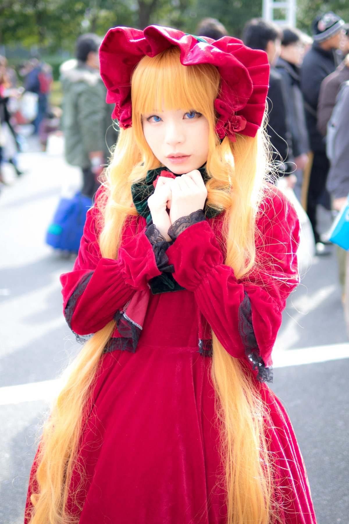 1girl blonde_hair blue_eyes blurry blurry_background blurry_foreground bonnet depth_of_field dress lips long_hair long_sleeves looking_at_viewer outdoors photo red_dress shinku solo solo_focus